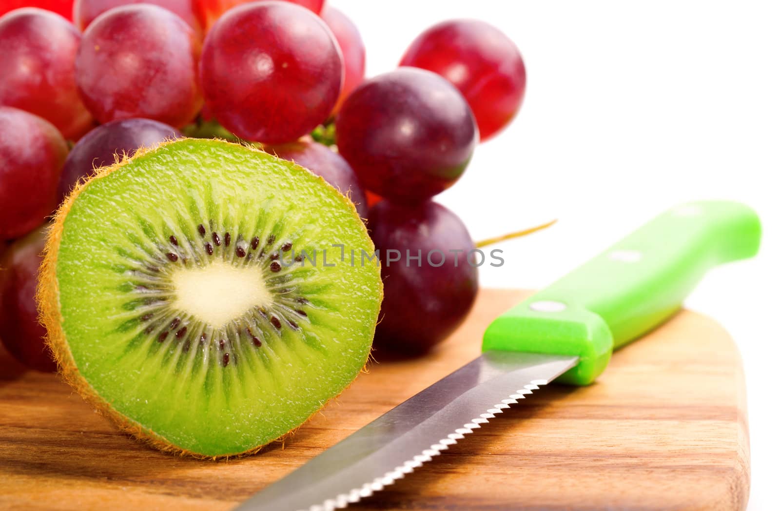 Single cross section of kiwi on grapes background, over white