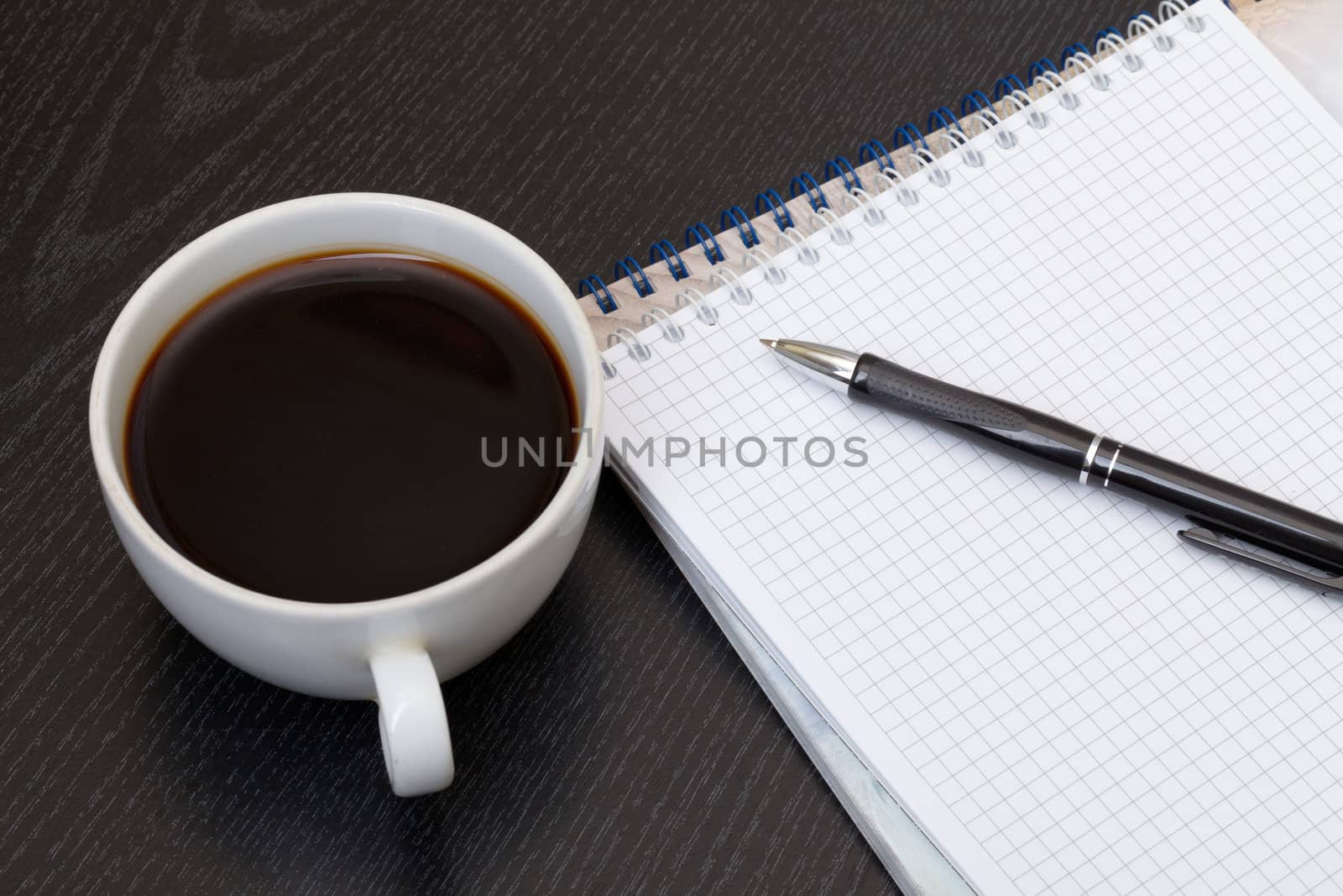 Coffee cup, spiral notebook and pen on the wooden table