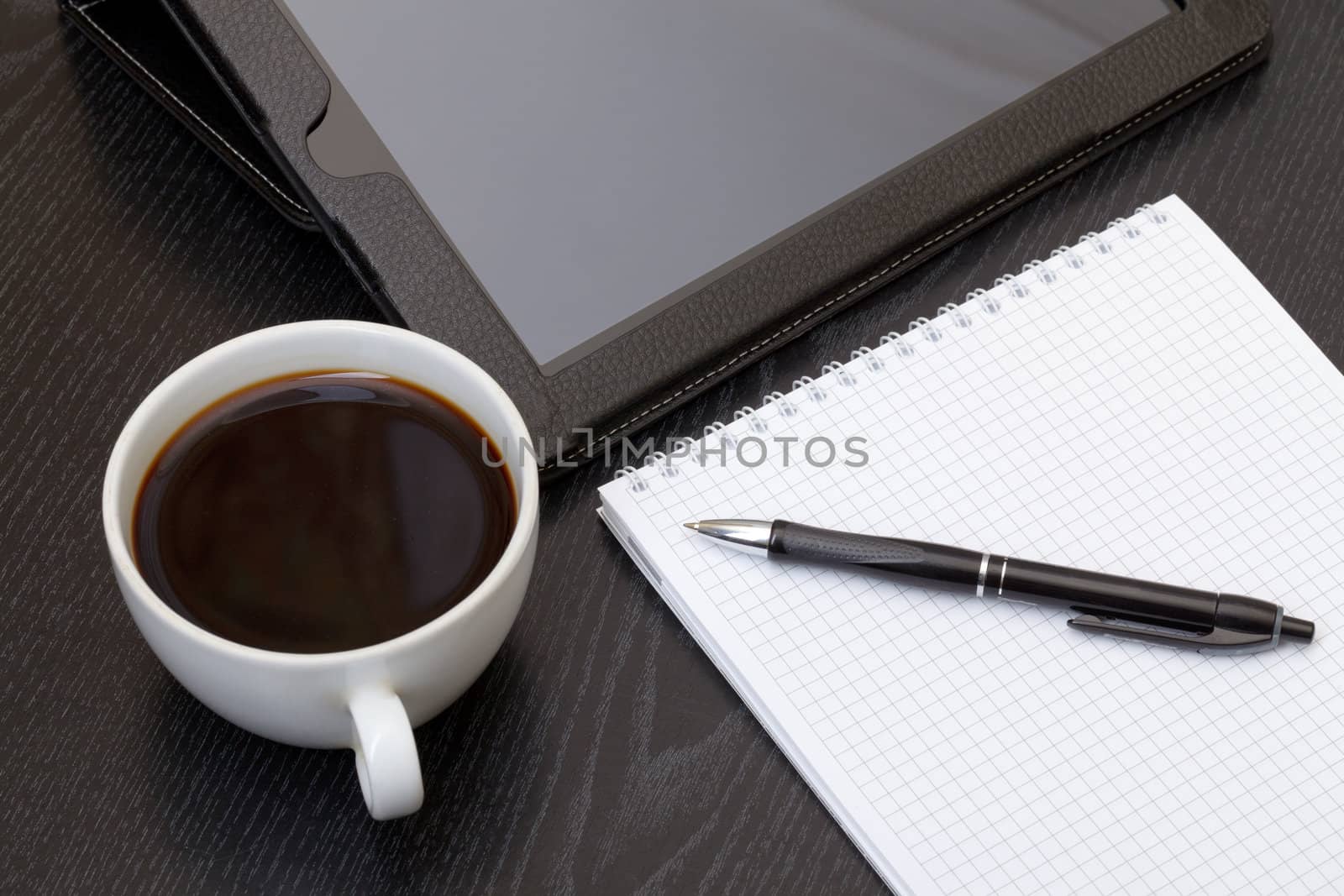 Coffee cup, tablet, spiral notebook and pen on the wooden table