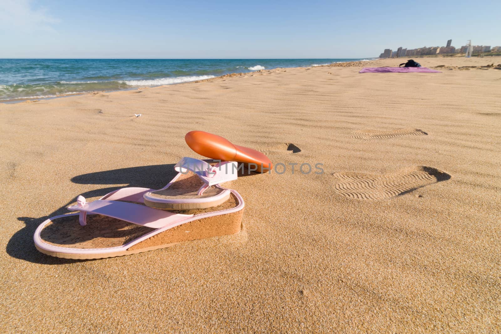 Sandals and sunscreen on a sunny sand beach