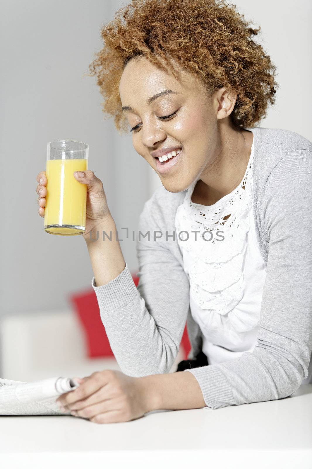 Beautiful young black woman reading a newspaper while enjoying fresh juice