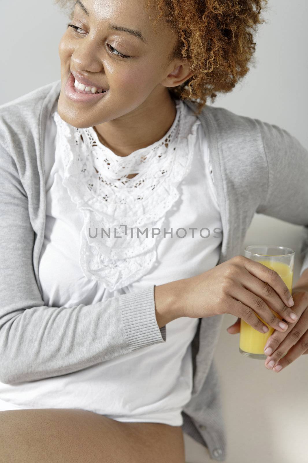 Beautiful young black woman enjoying a glass of fresh juice while sitting on sofa