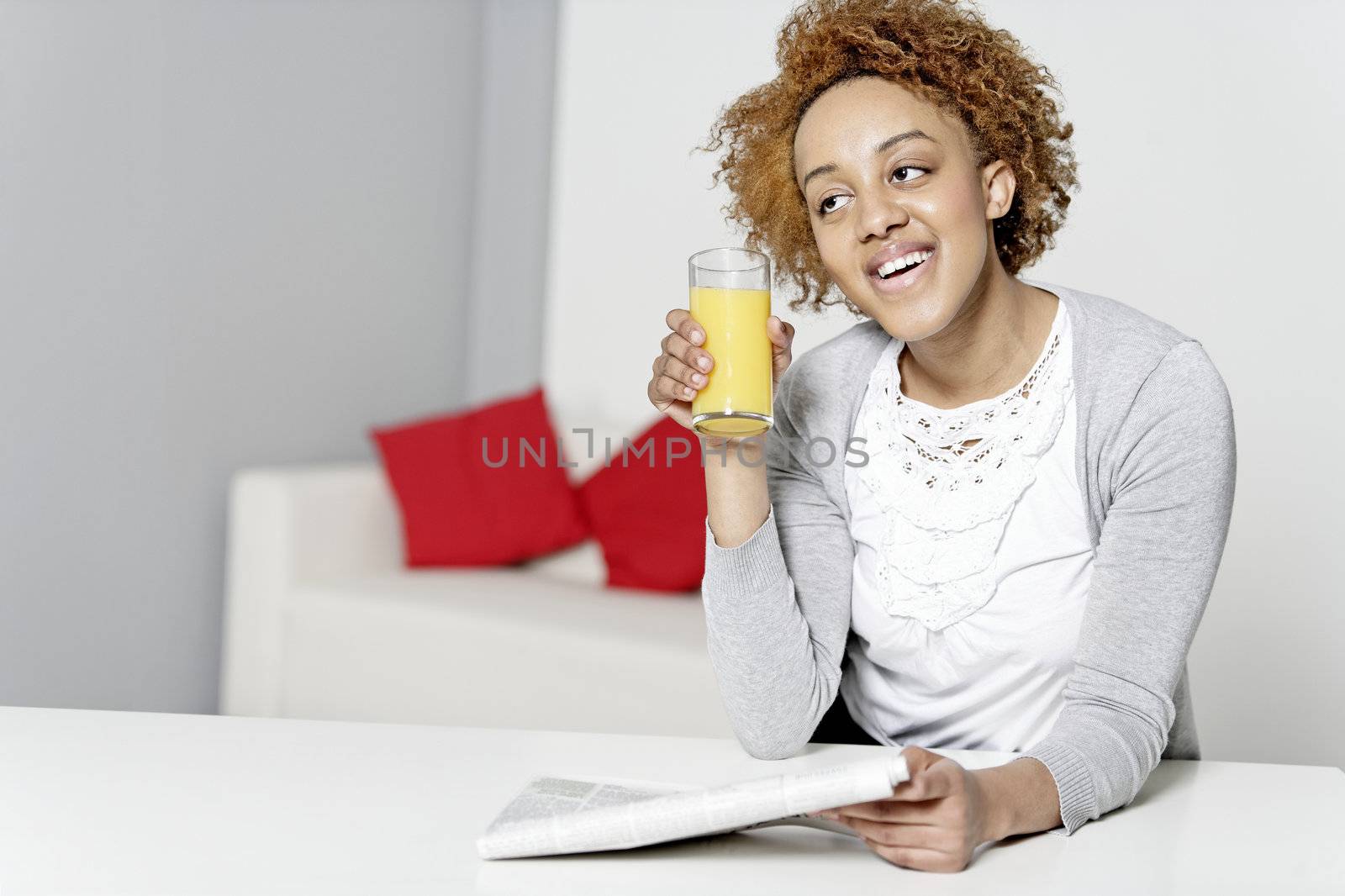 Beautiful young black woman reading a newspaper while enjoying fresh juice