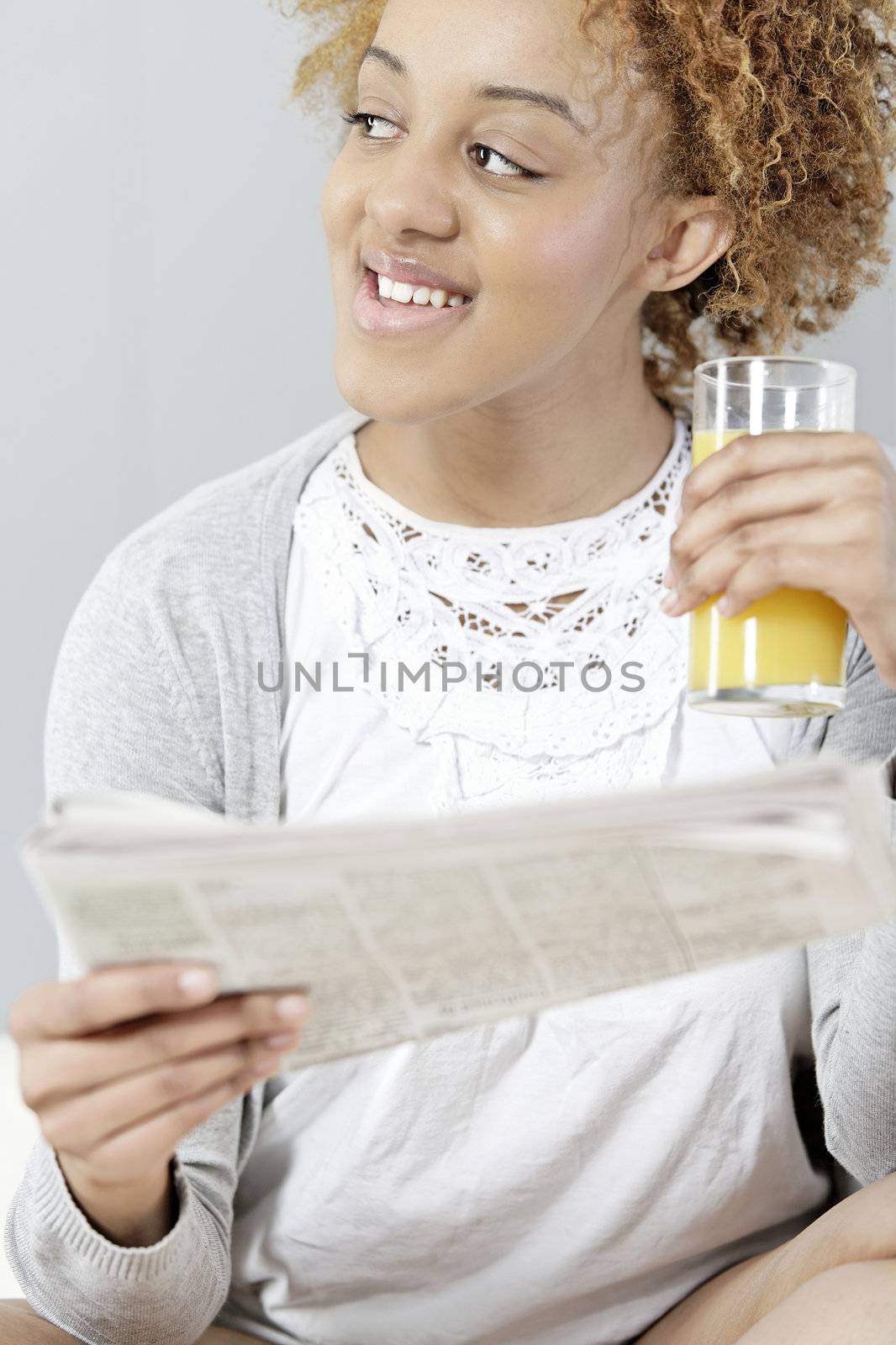 Beautiful young black woman enjoying a newspaper and a glass of juice