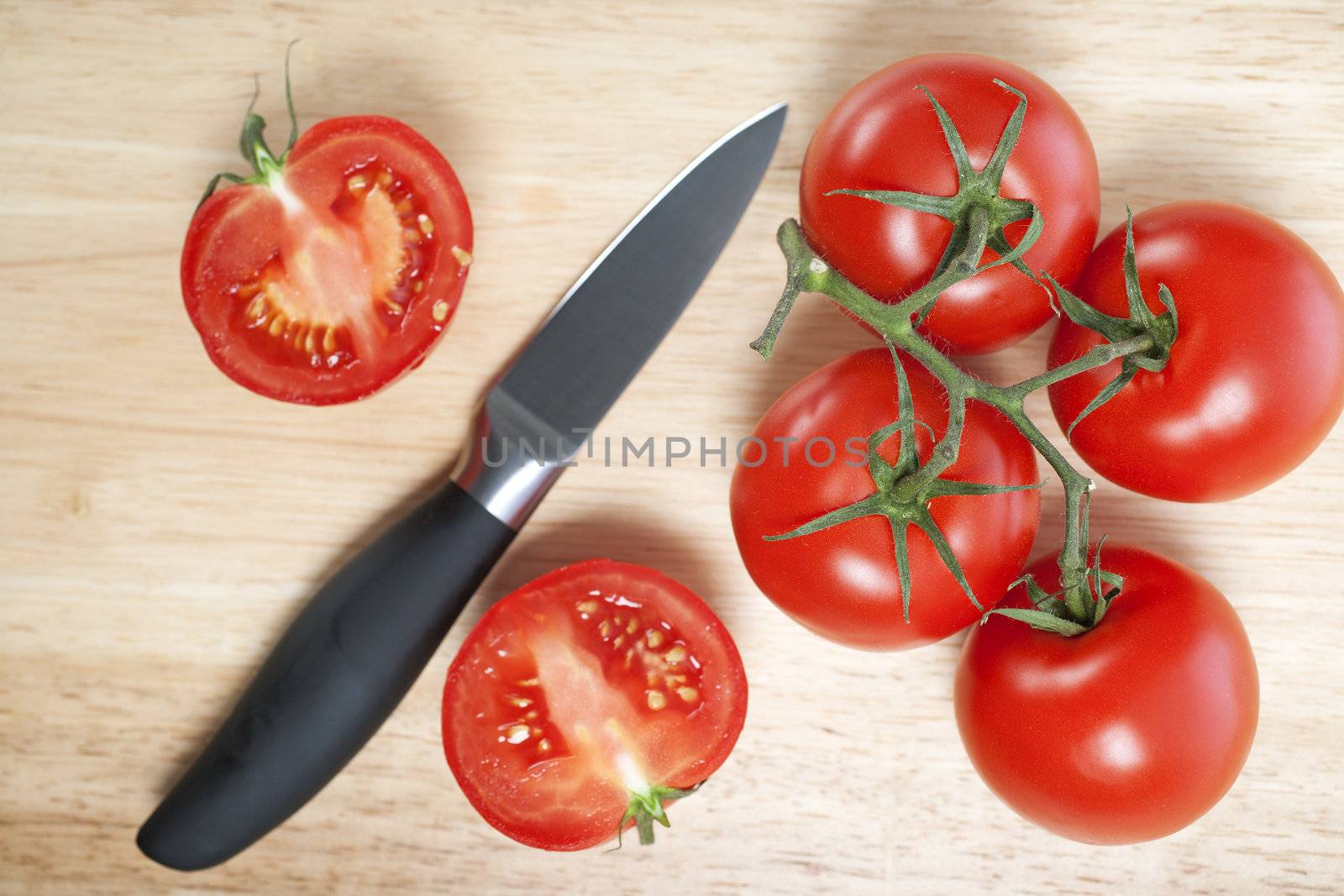 Fresh tomatoes being sliced on a wooden chopping board with knife