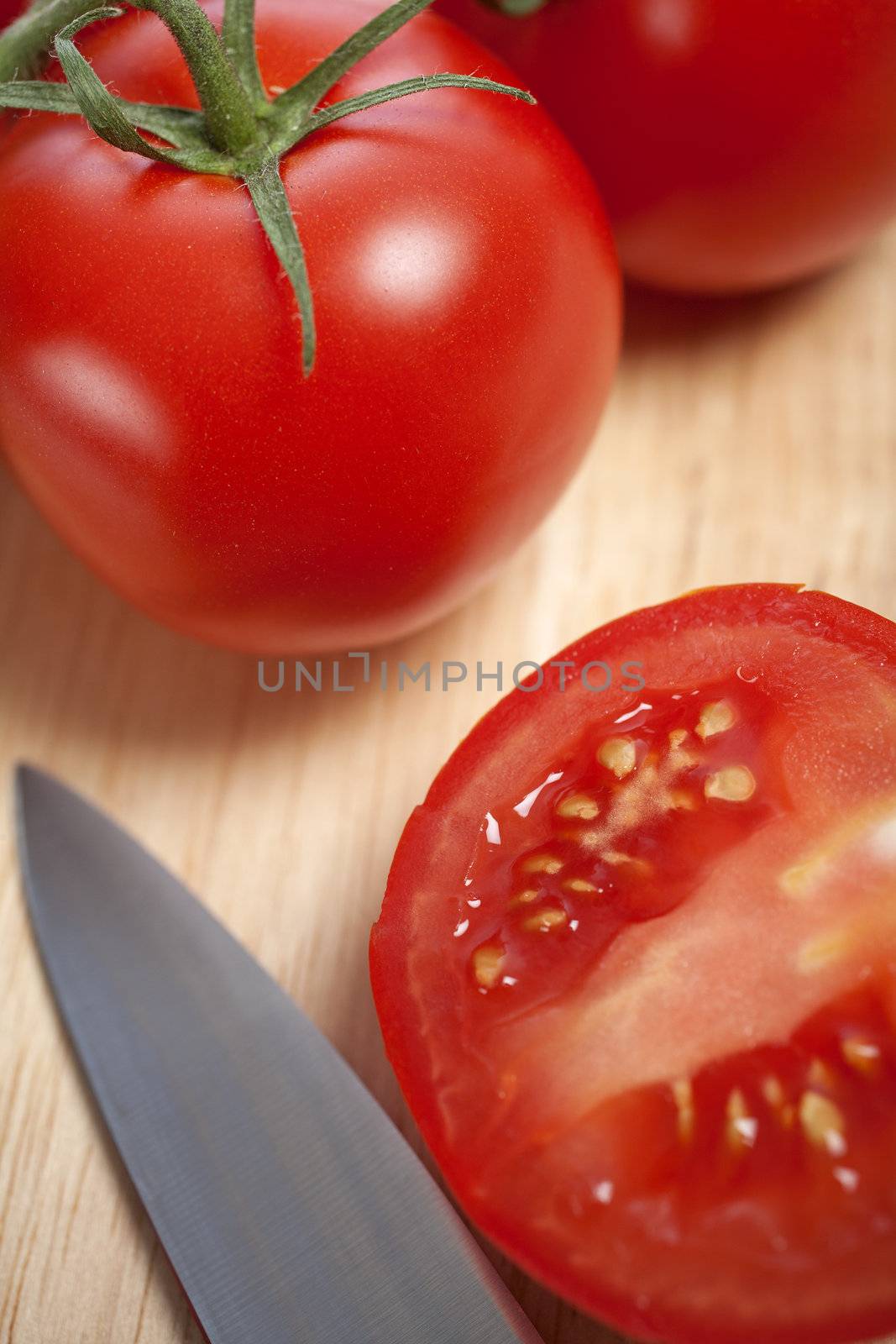 Fresh tomatoes being sliced on a wooden chopping board with knife
