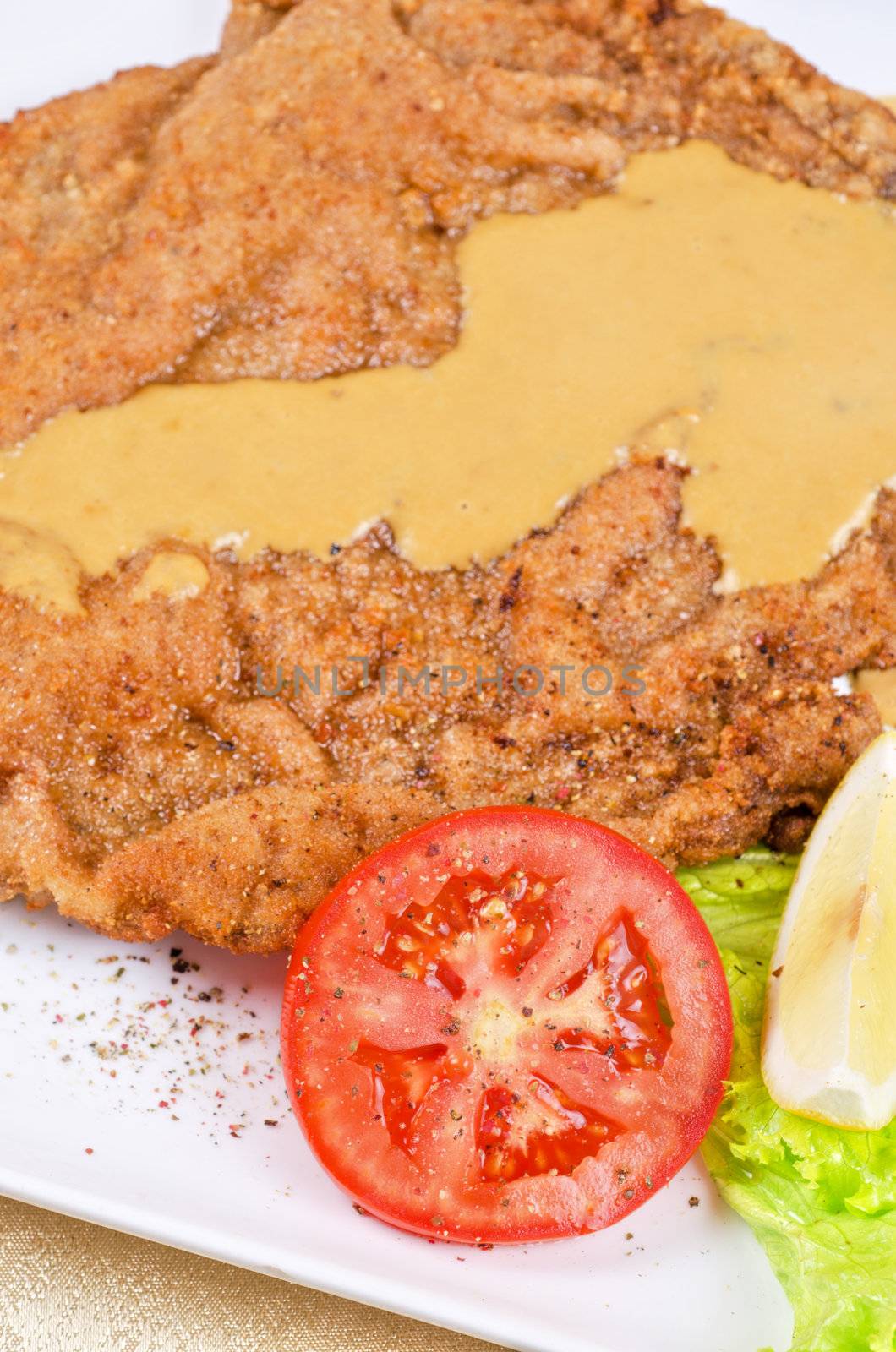 Delicious Schnitzel with lemon, tomato, lettuce and sauce.