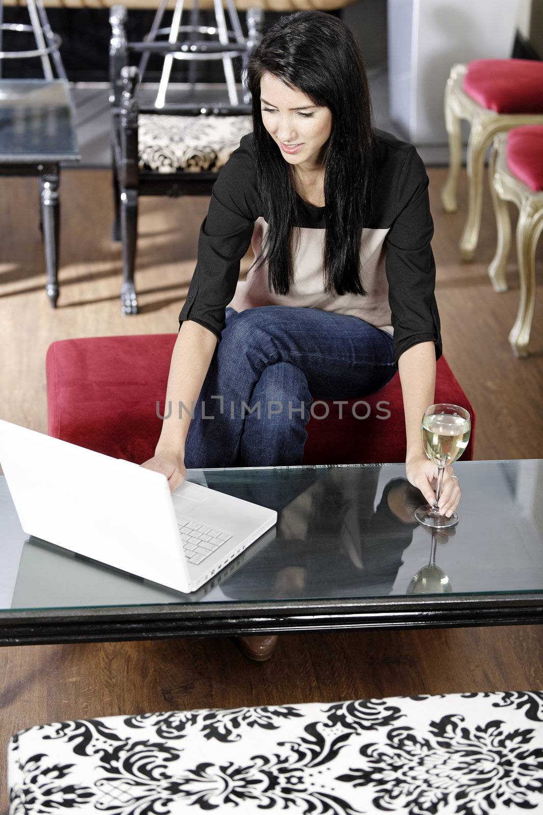 Beautiful young woman chatting with friends on her laptop while enjoying a glass of wine in a bar