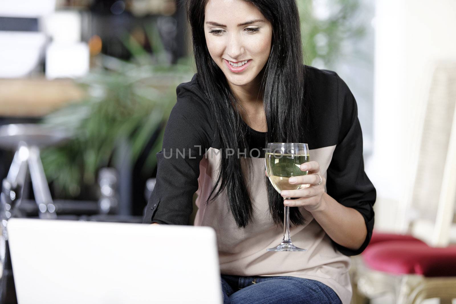 Beautiful young woman chatting with friends on her laptop while enjoying a glass of wine in a bar