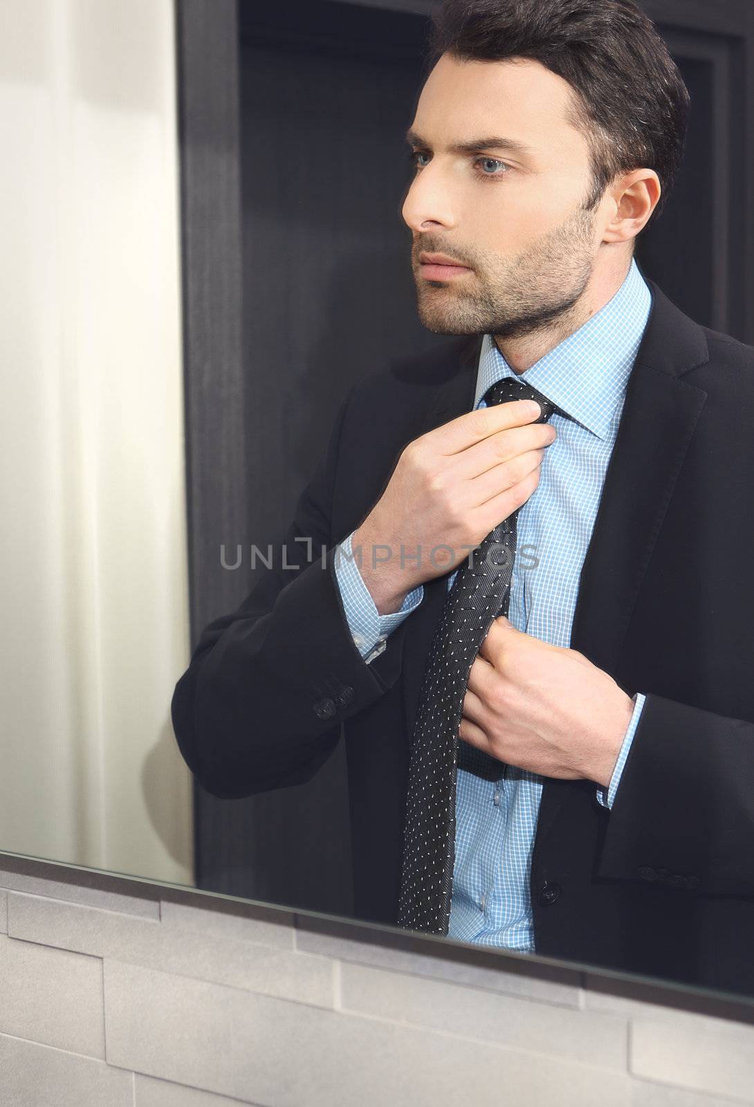 The young man looks at himself in the mirror and adjusts his tie