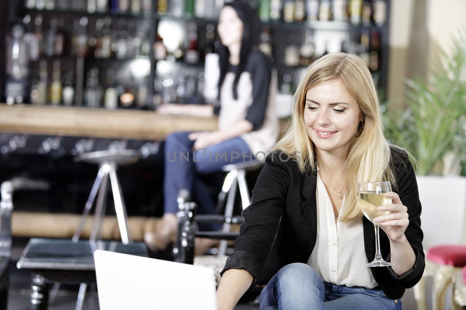 Beautiful young woman chatting with friends on her laptop while enjoying a glass of wine in a bar