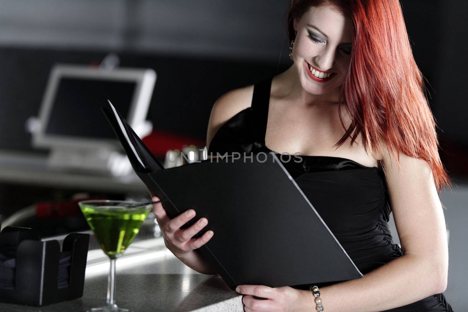 Attractive young woman reading from a wine list at the bar.