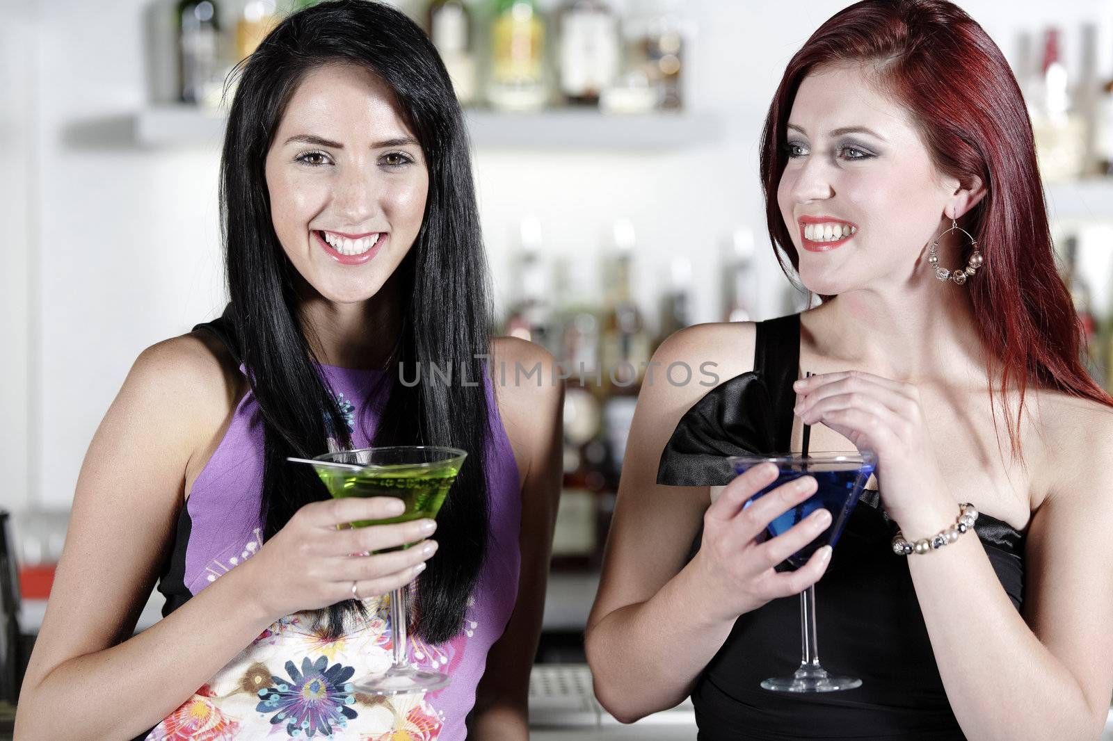 Two beautiful young woman chatting and drinking cocktails at a nightclub or wine bar.