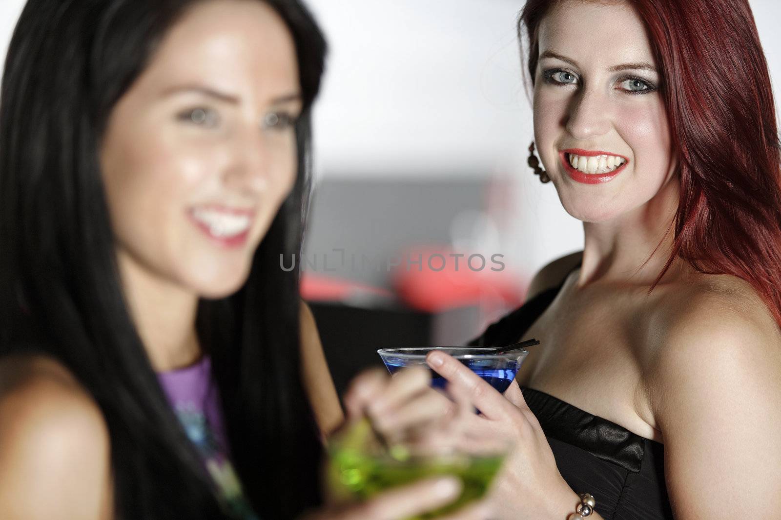 Two beautiful young woman chatting and drinking cocktails at a nightclub or wine bar.