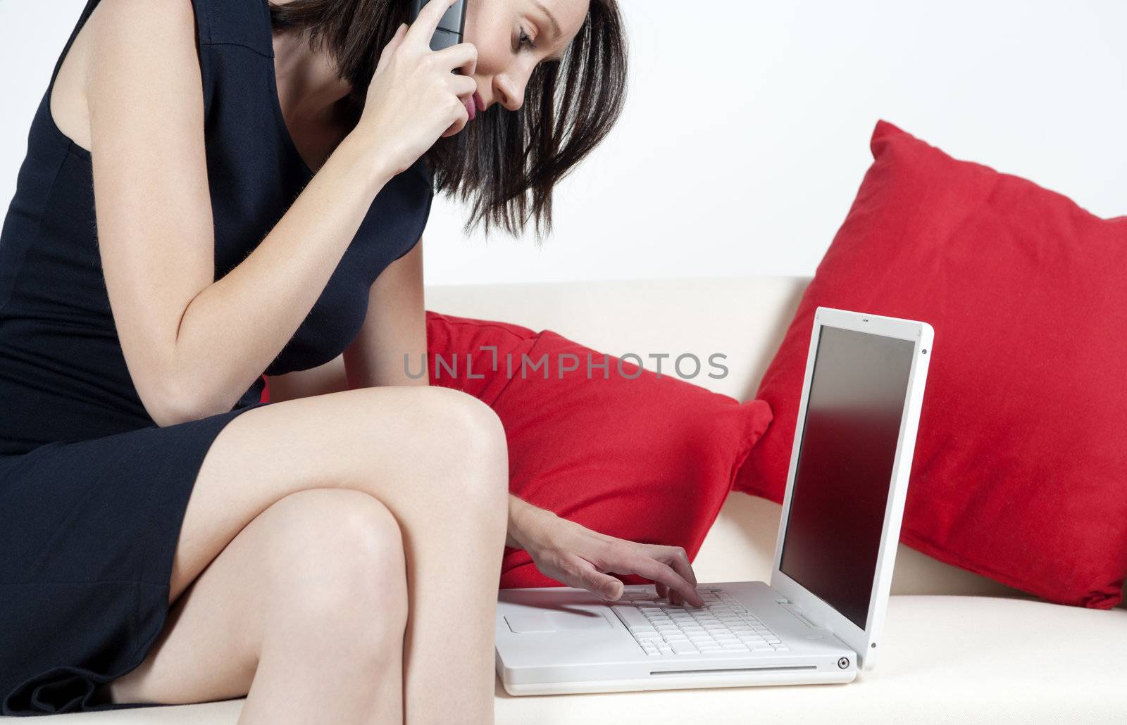 Woman in black dress working on laptop and chatting on the phone