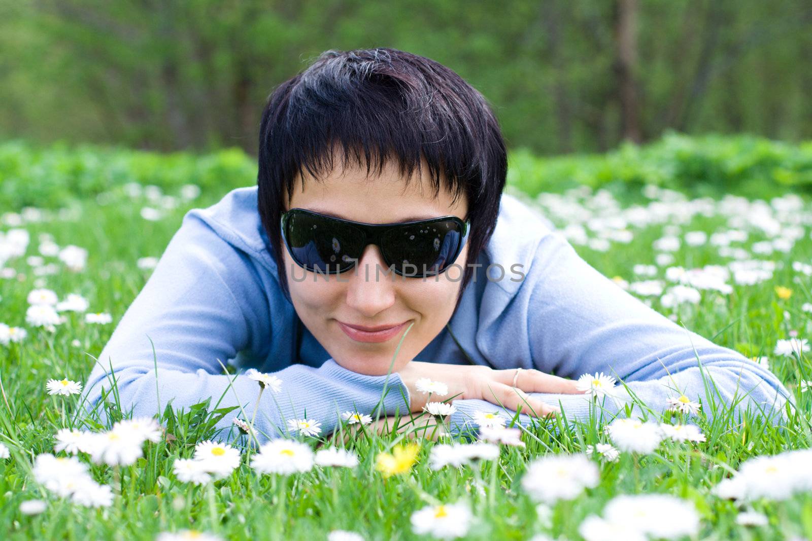 Young woman in sunglasses is lying on the flowering meadow