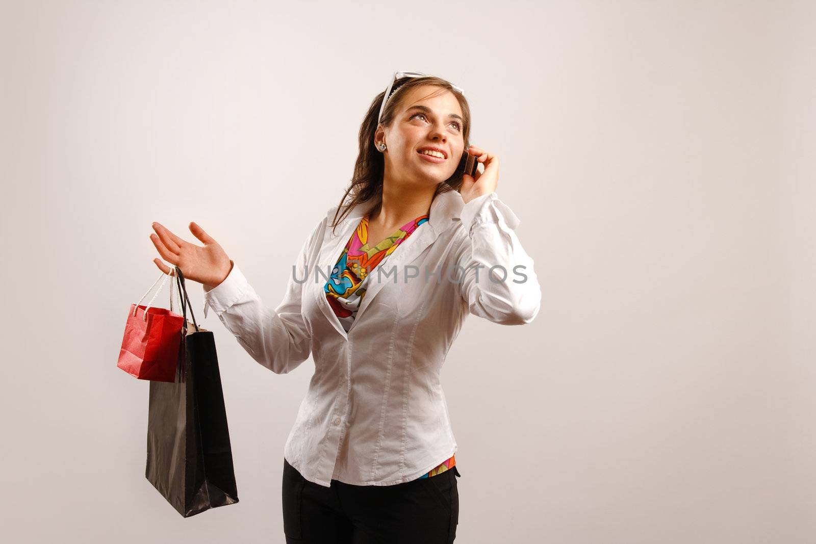 Modern looking young woman wearing white jacket talking on the phone and holding shopping bags