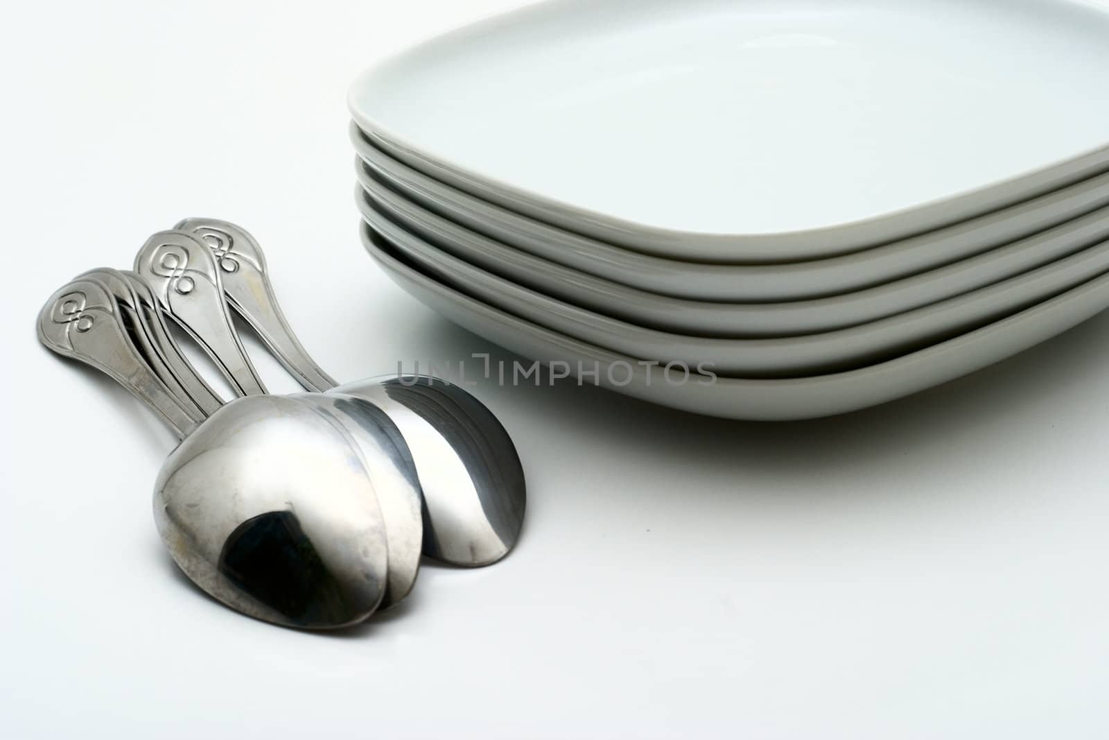 Pile of white plates and shining spoons on a white background. Preparation for table layout.