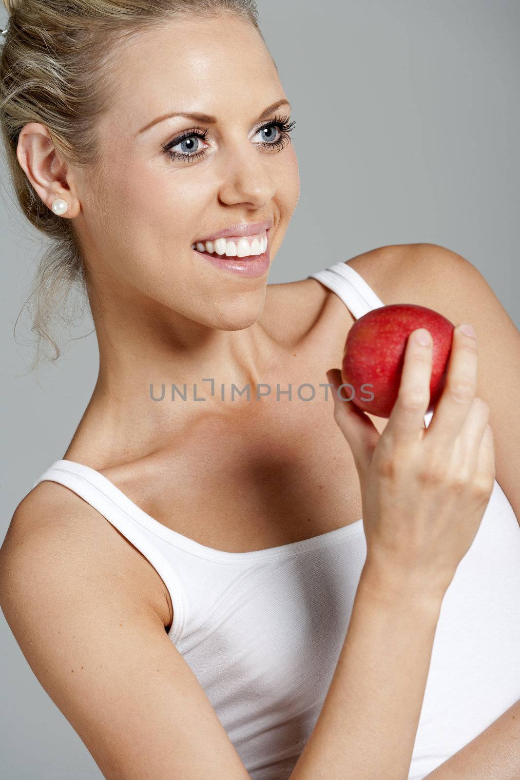 Beautiful young woman eating an apple wearing a white vest top