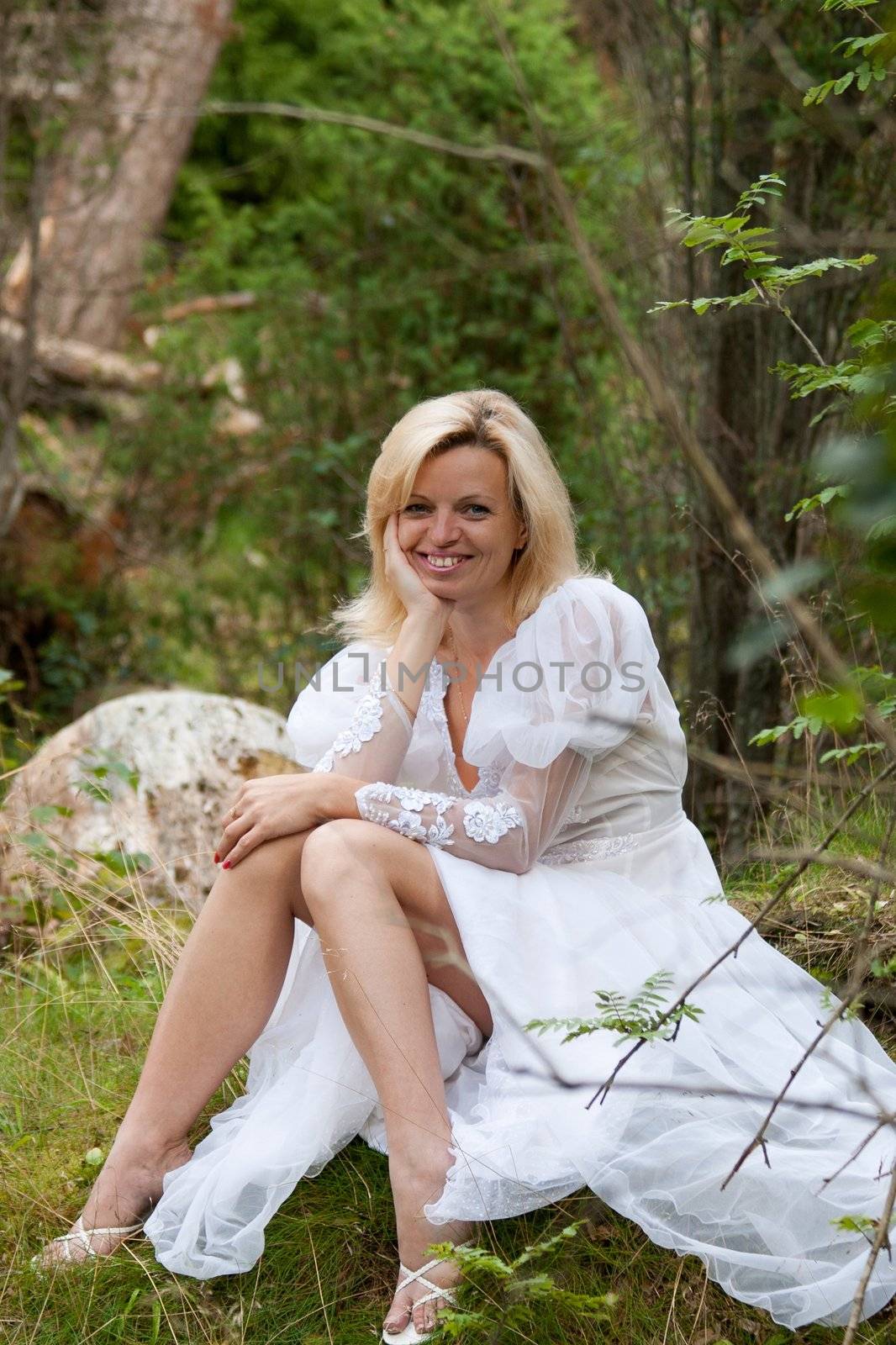 smiling woman in white dress sitting in the woods