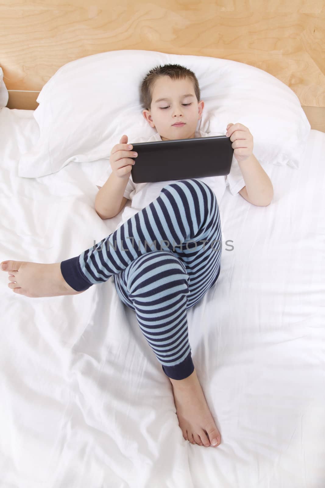 Elementry school boy reading his tablet before he goes to bed