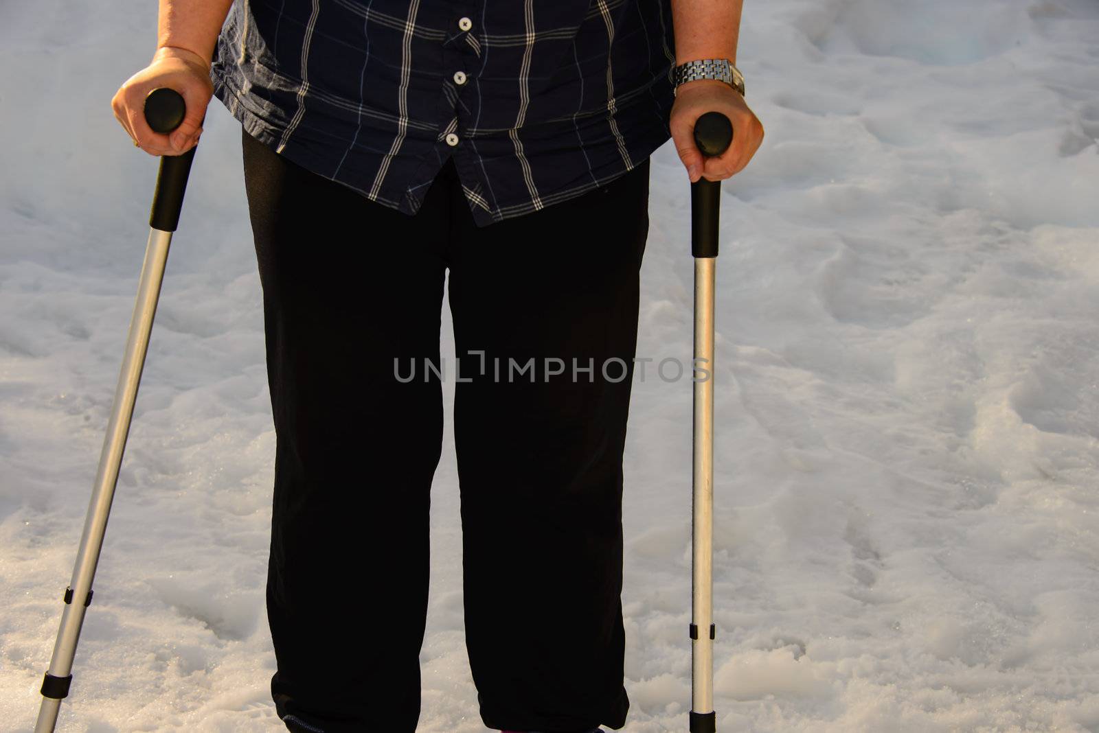 An obese woman waking with crutches outdour in the snow.