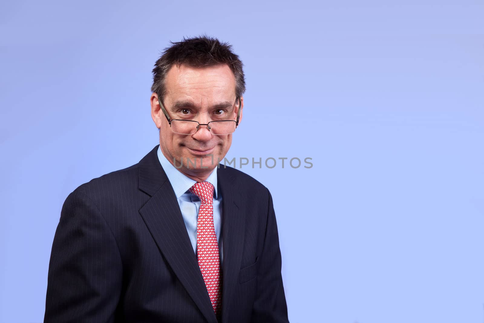 Smiling Business Man in Suit Looking Over Glasses on Blue Background