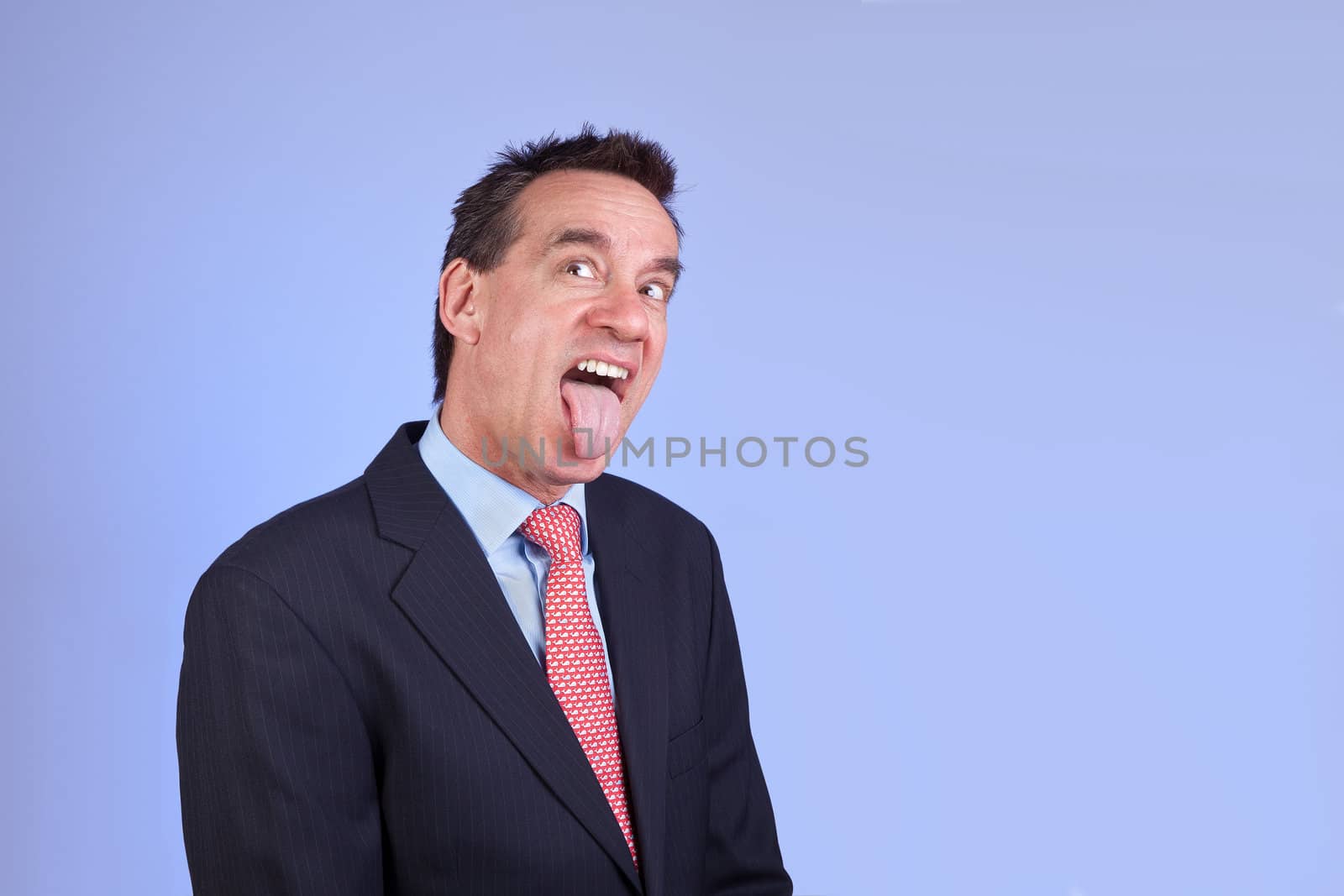 Attractive Business Man in Suit Sticking out Tongue on Blue Background
