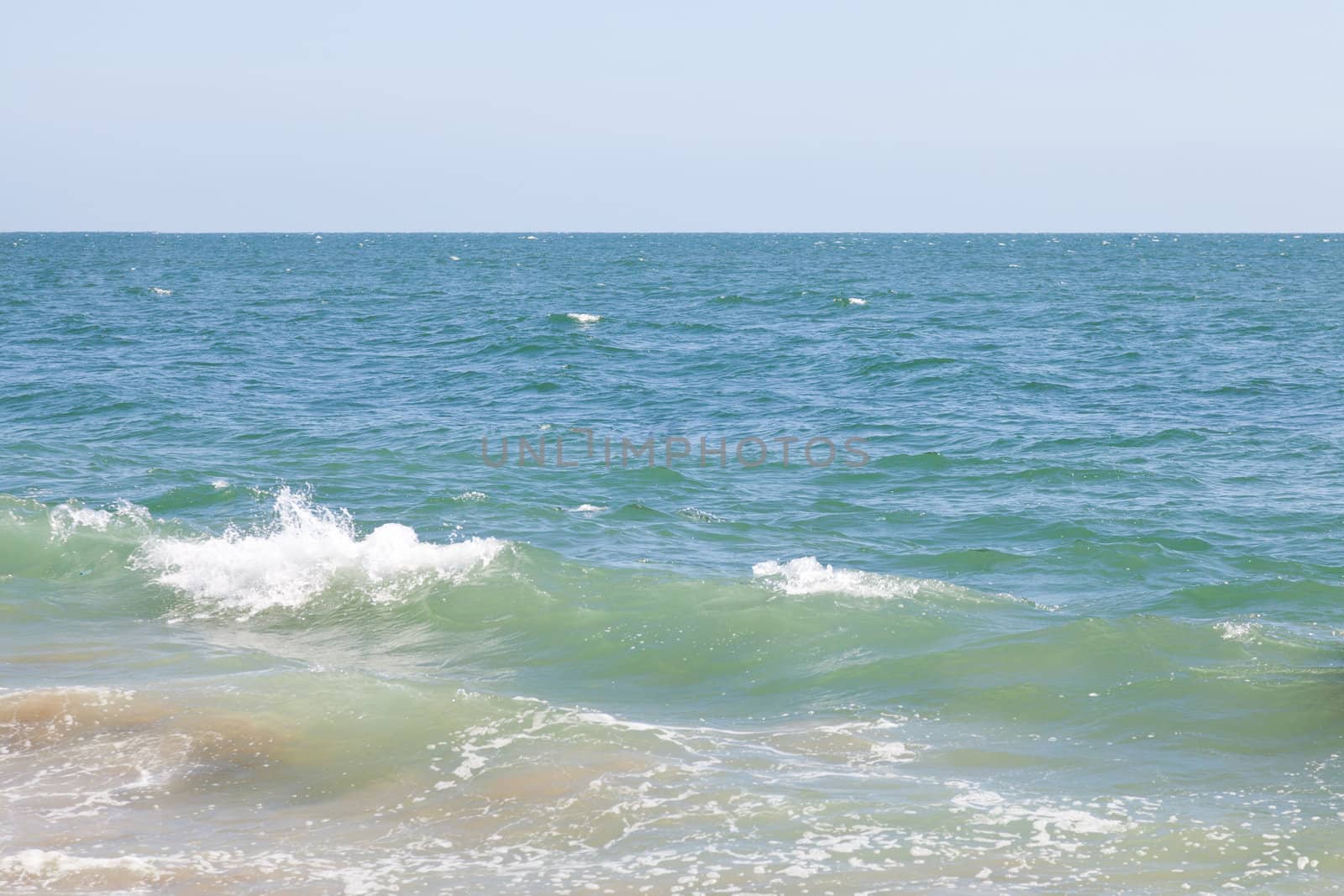 Abstract of a calm blue-green ocean with small breaking wave on the left,