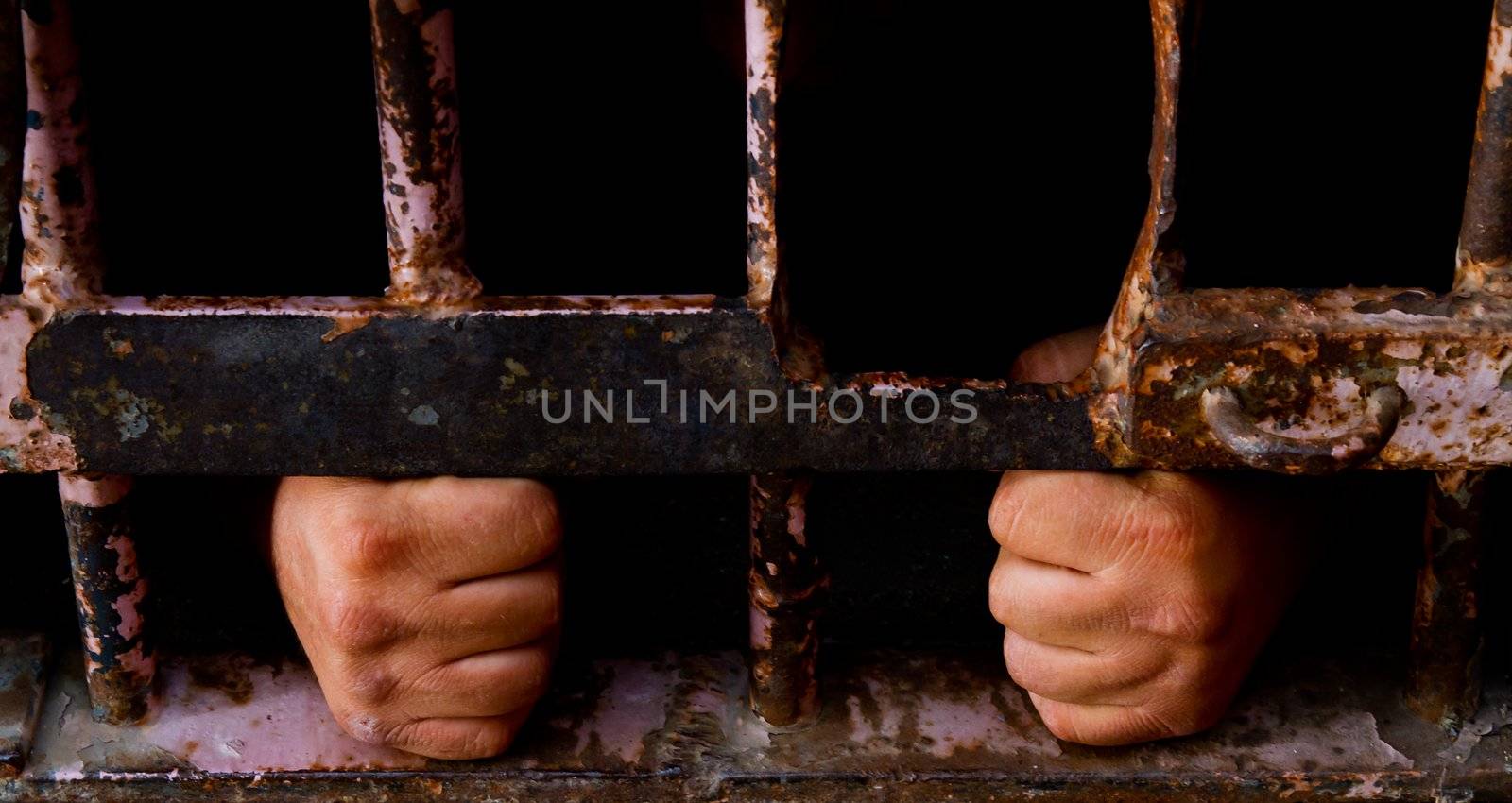 Mans hands grabbing onto old rusted bars with face hidden in darknes