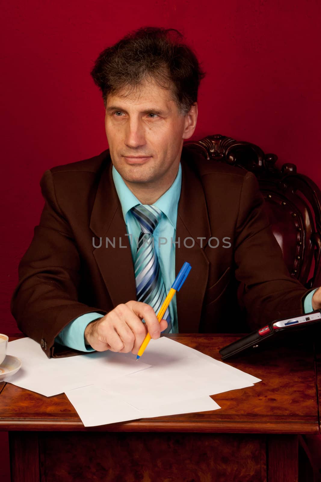 Portrait of middle-aged man working in his home at his desk on a background of red wallpaper