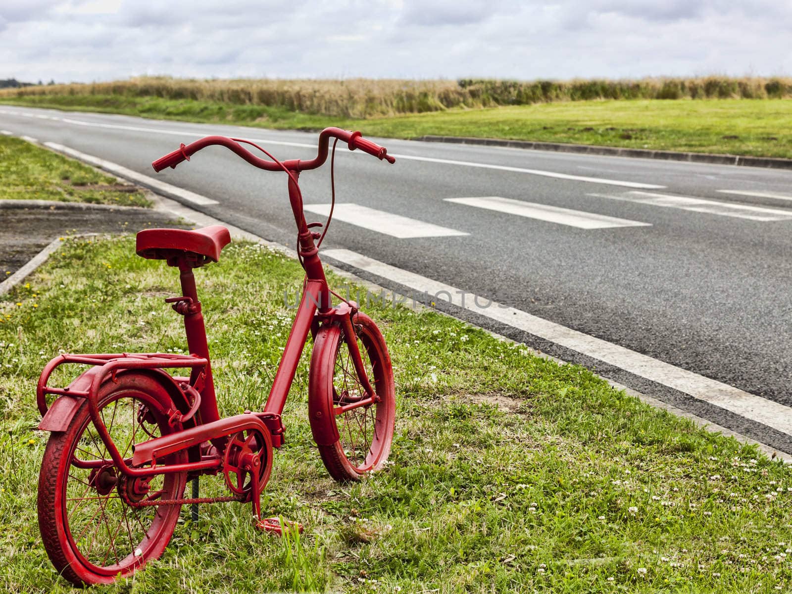 Small rusty bicycle painted in red on a roadside in a rural area.