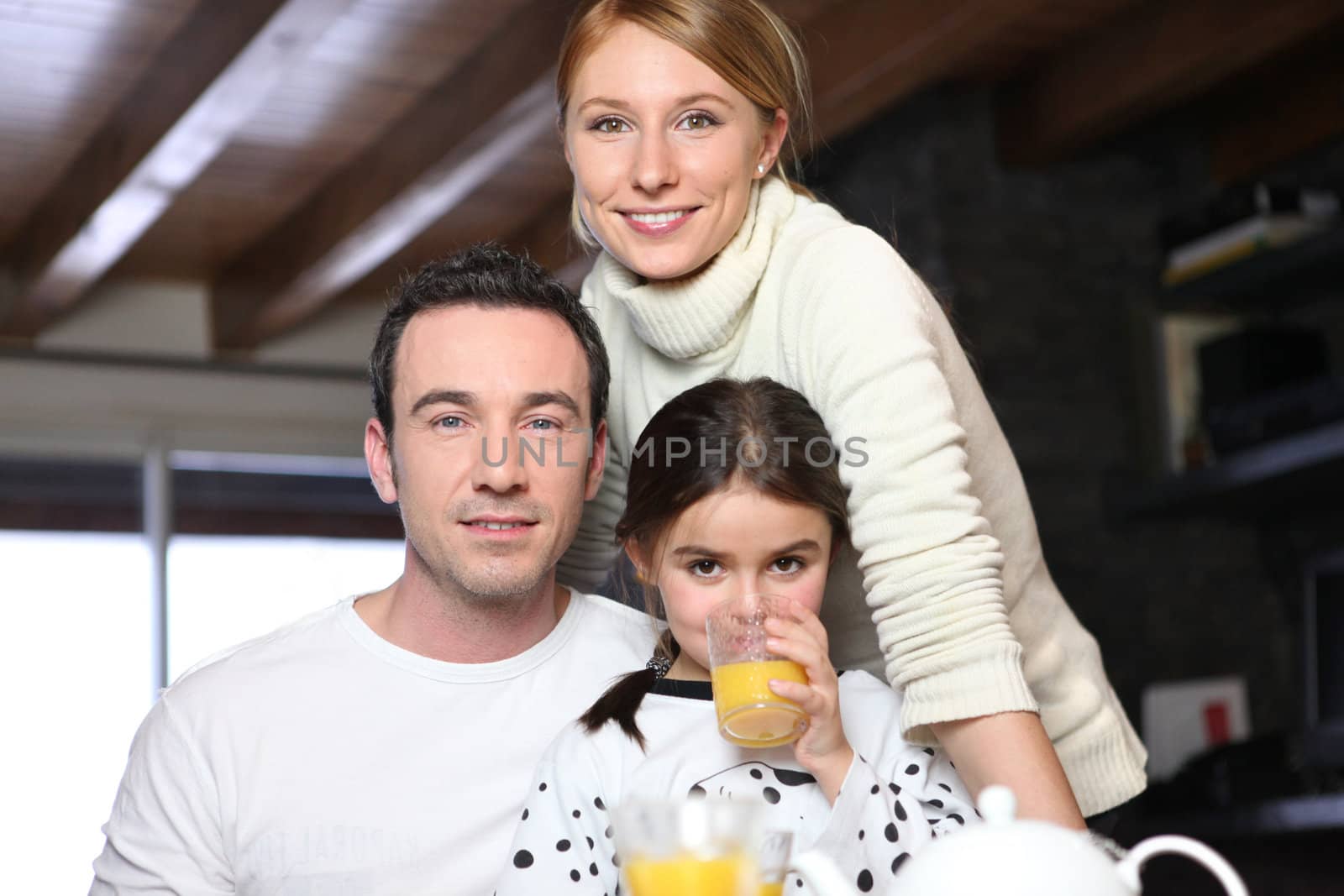 Young girl drinking a glass of orange juice while posing for the camera with her parents