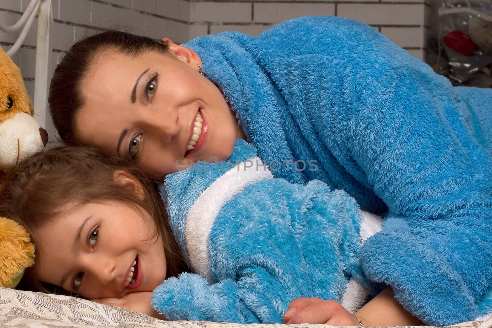 Mom and daughter in the same blue terry robe lying on the bed