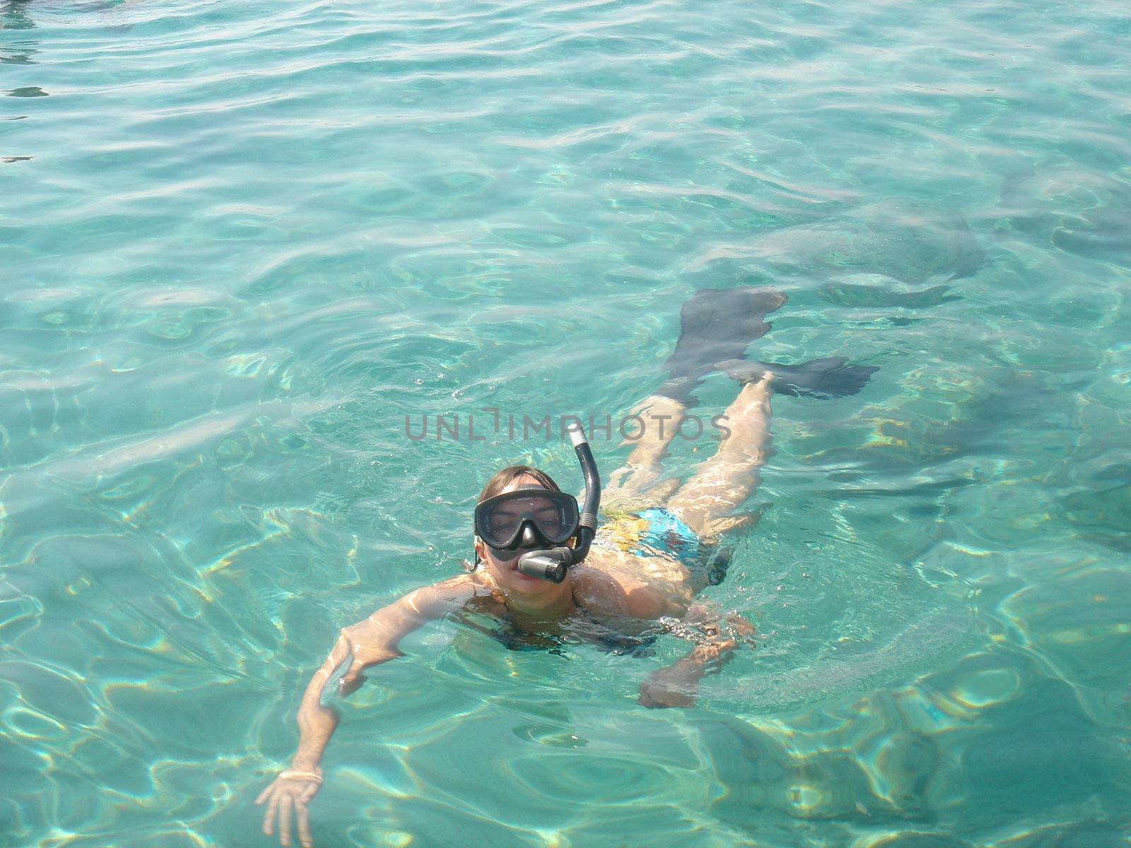 Girl with snorkel and flippers in sea water looks at camera                              