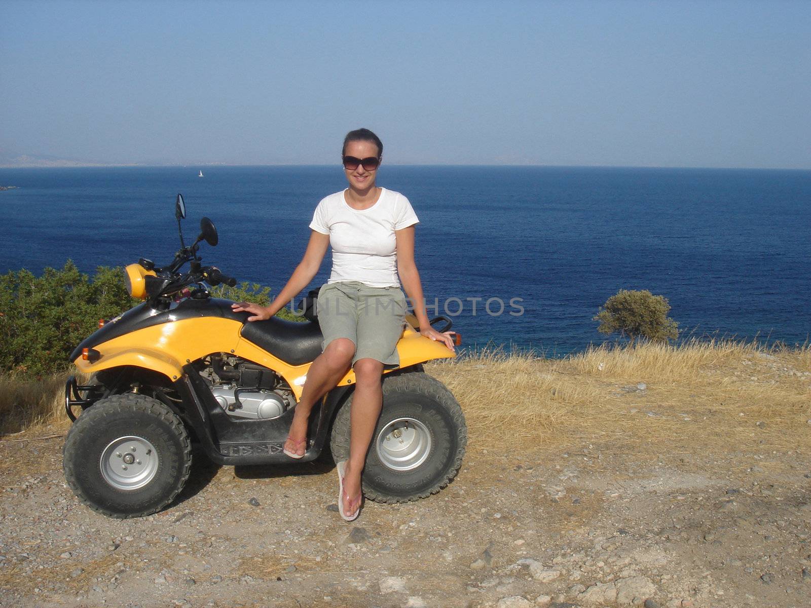 Pretty girl on quadricycle against blue sea                               