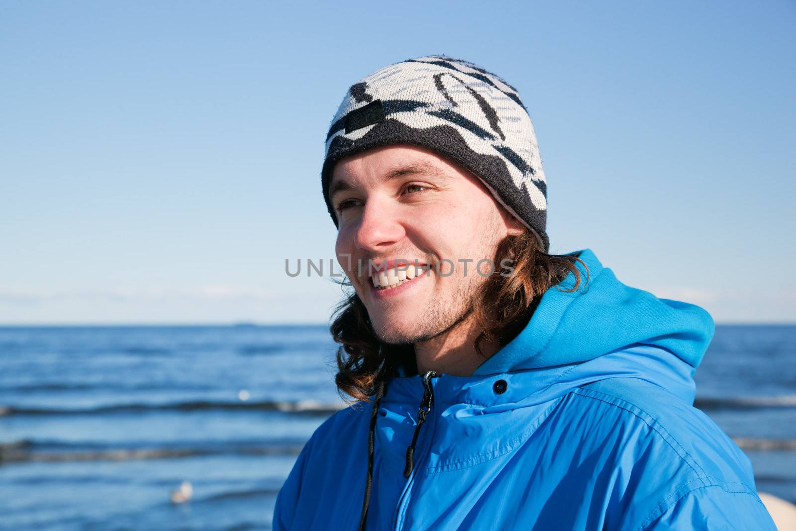 Young man smiling portrait on the beach in a sunny cold day