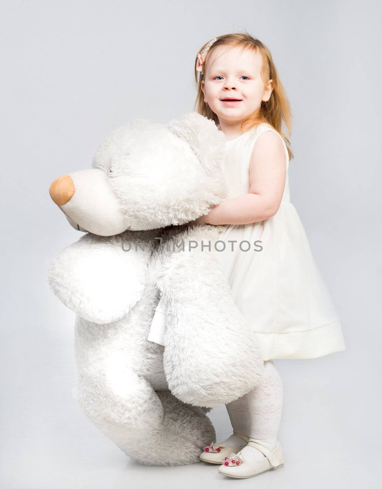 Little girl with toy bear on light background
