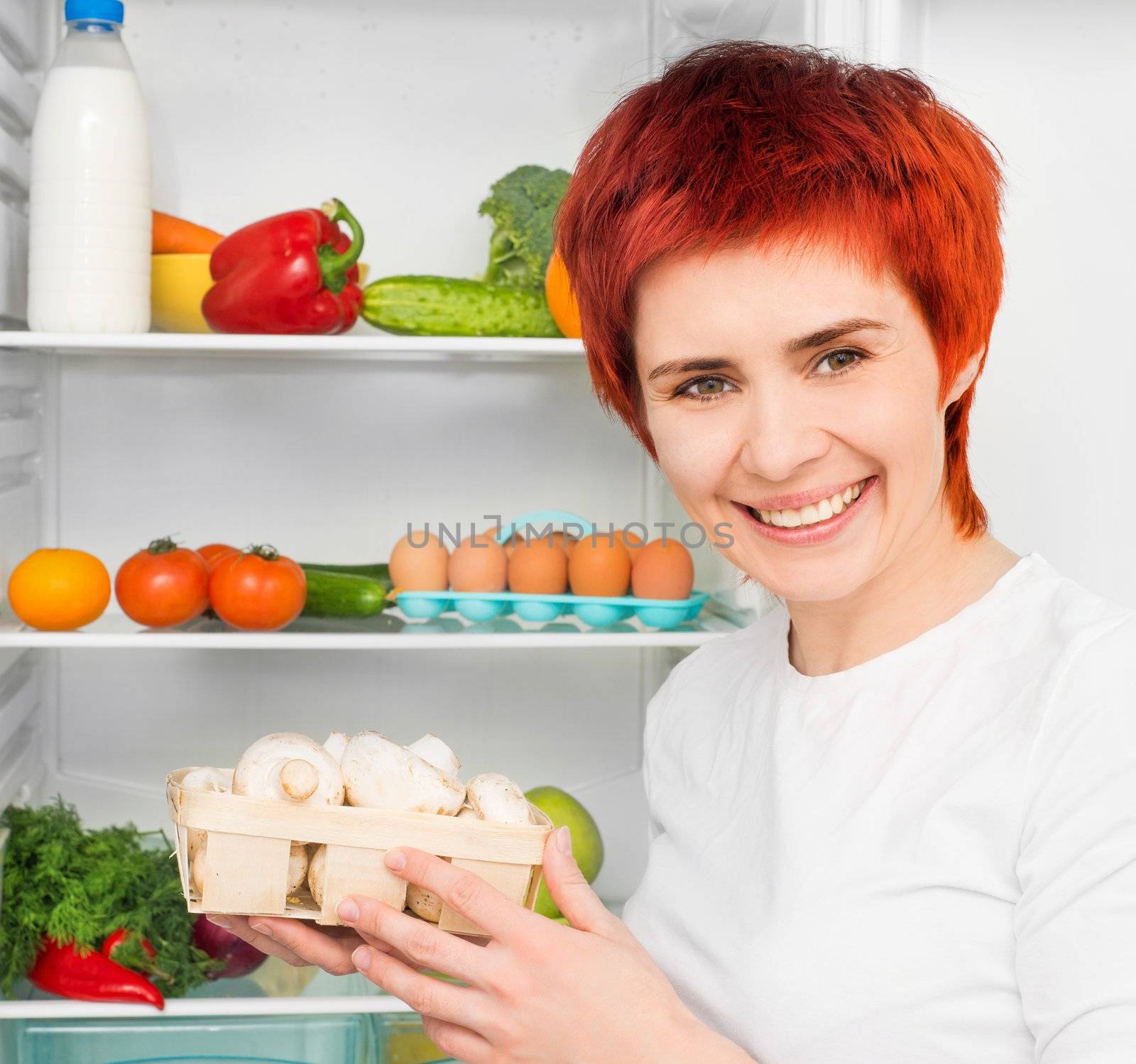young smiling woman with mushroom against the refrigerator with food