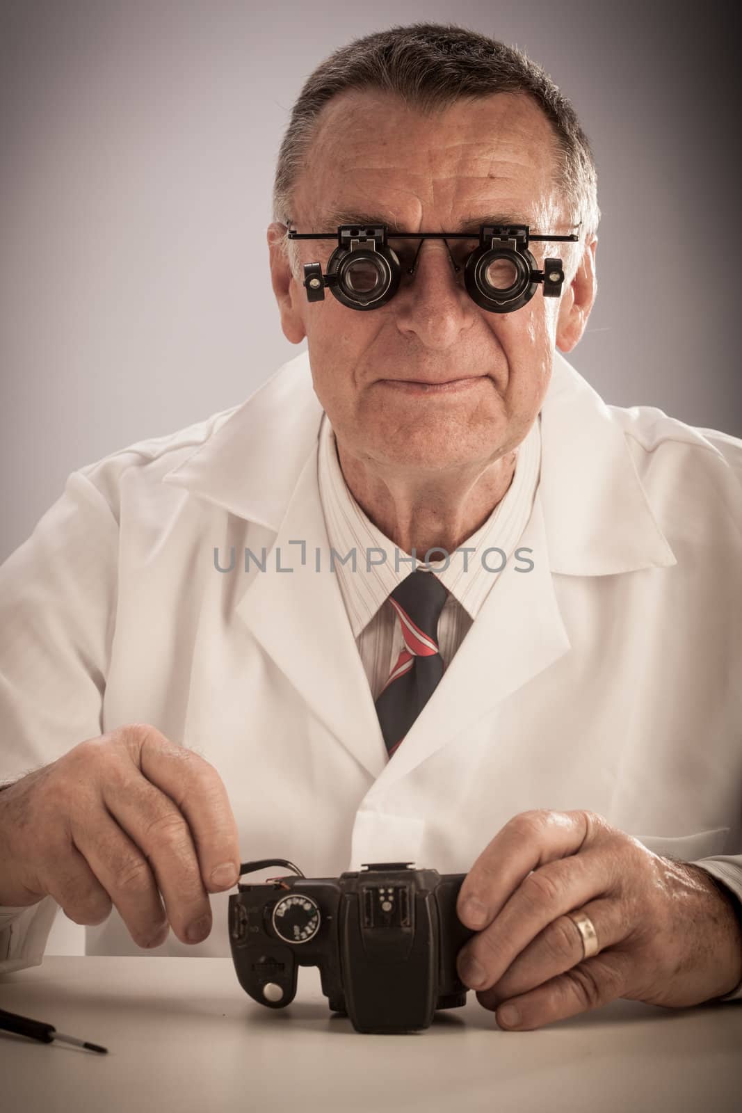 An older male wearing a white lab coat and repairing electronic equipments, like a technician or a repair man.