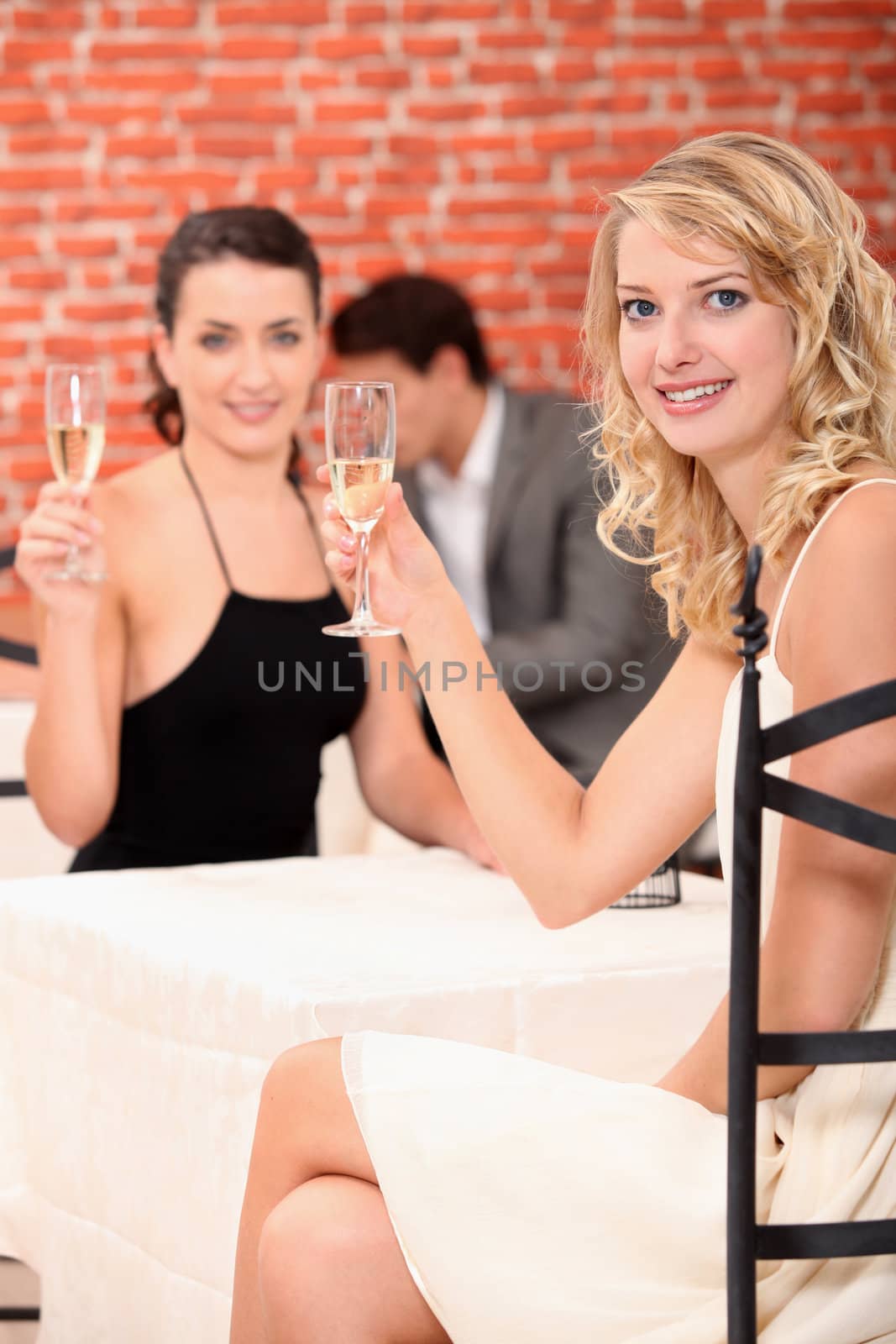 Two female friends drinking champagne in restaurant by phovoir