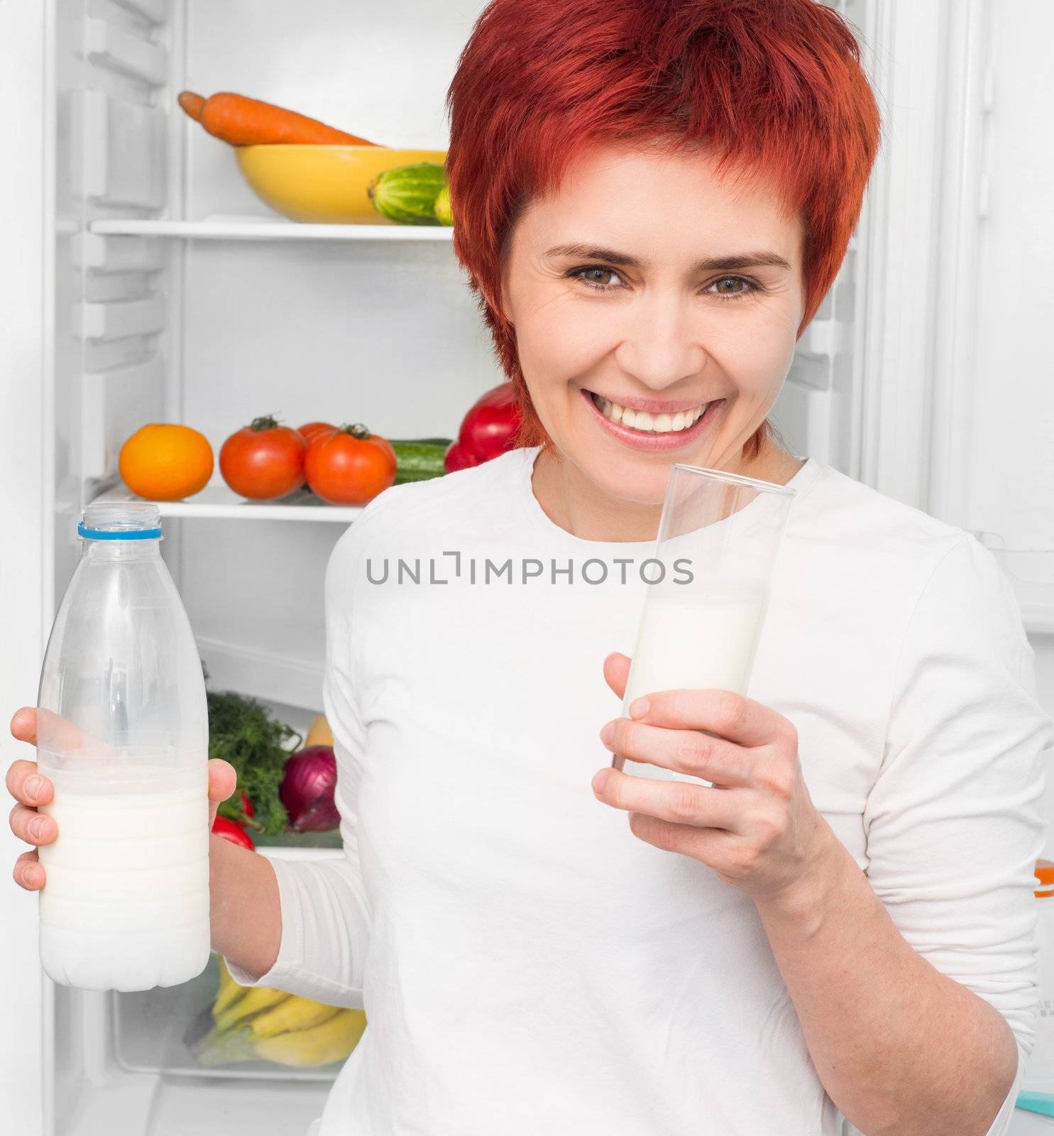 young woman with bottle milk against the refrigerator with food