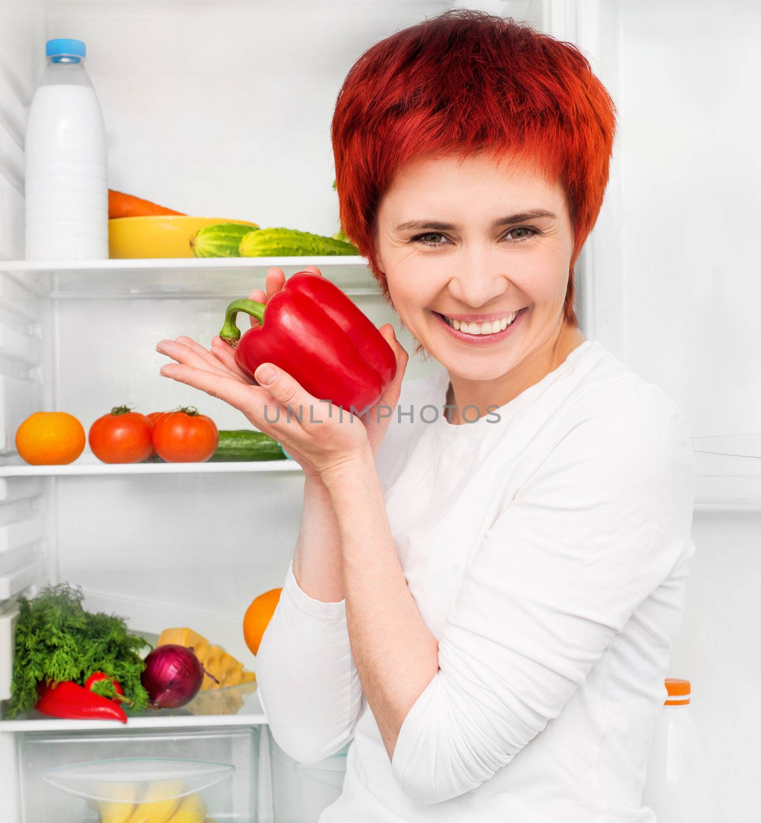 smiling girl with papper against the refrigerator with food