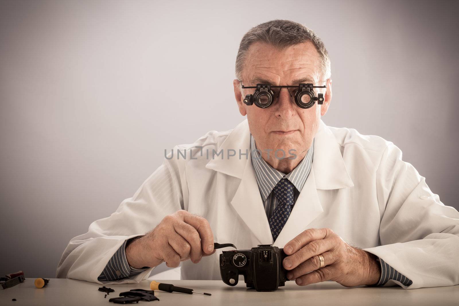 An older male wearing a white lab coat and repairing electronic equipments, like a technician or a repair man.