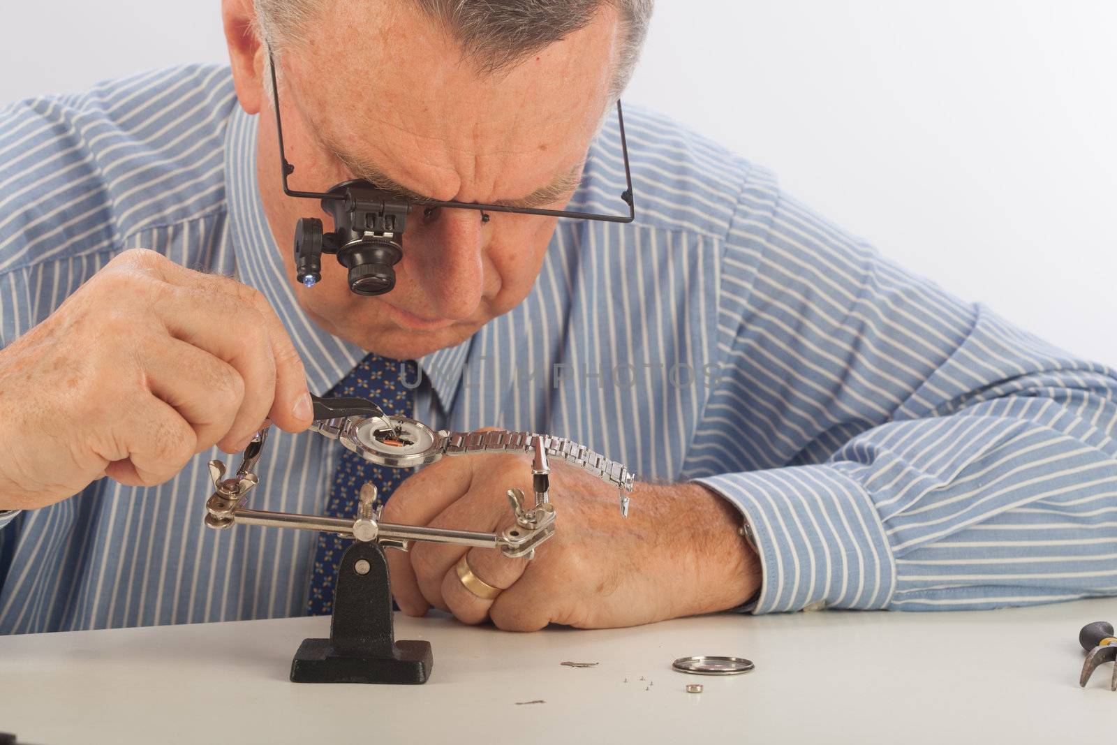 An older man wearing a shirt and tie, repairing a watch.