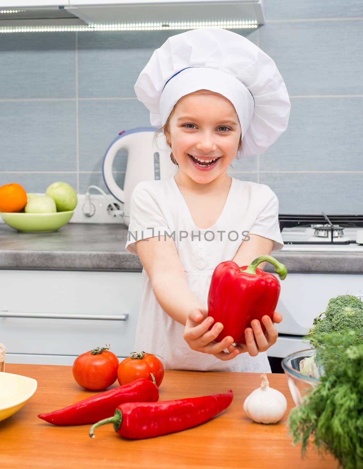 little smiling girl in a cap chef in the kitchen with Pepper