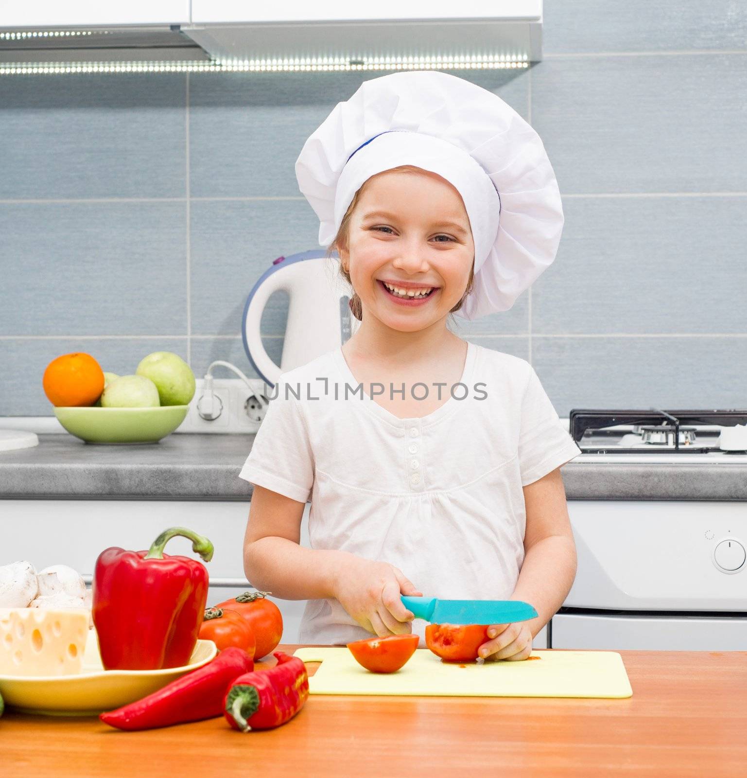 little girl in a cap chef in the kitchen cutting tomatoes