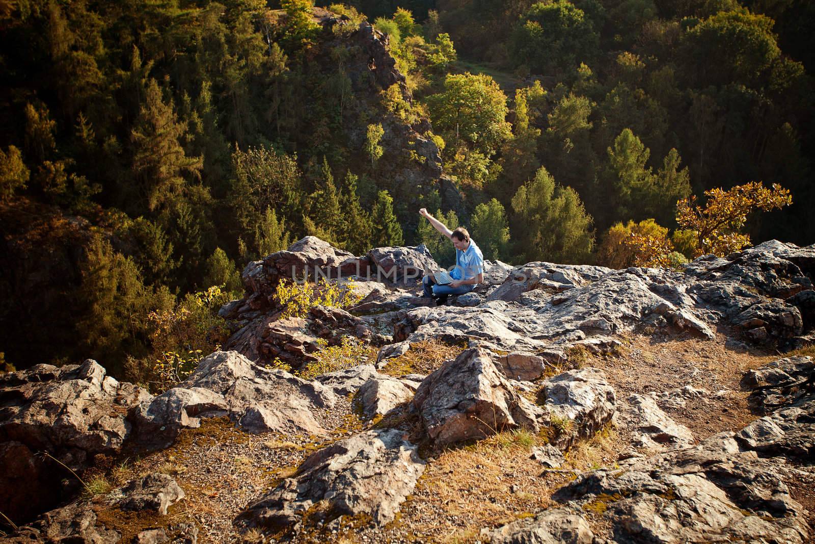 young man using laptop sitting on a rock slope by jannyjus