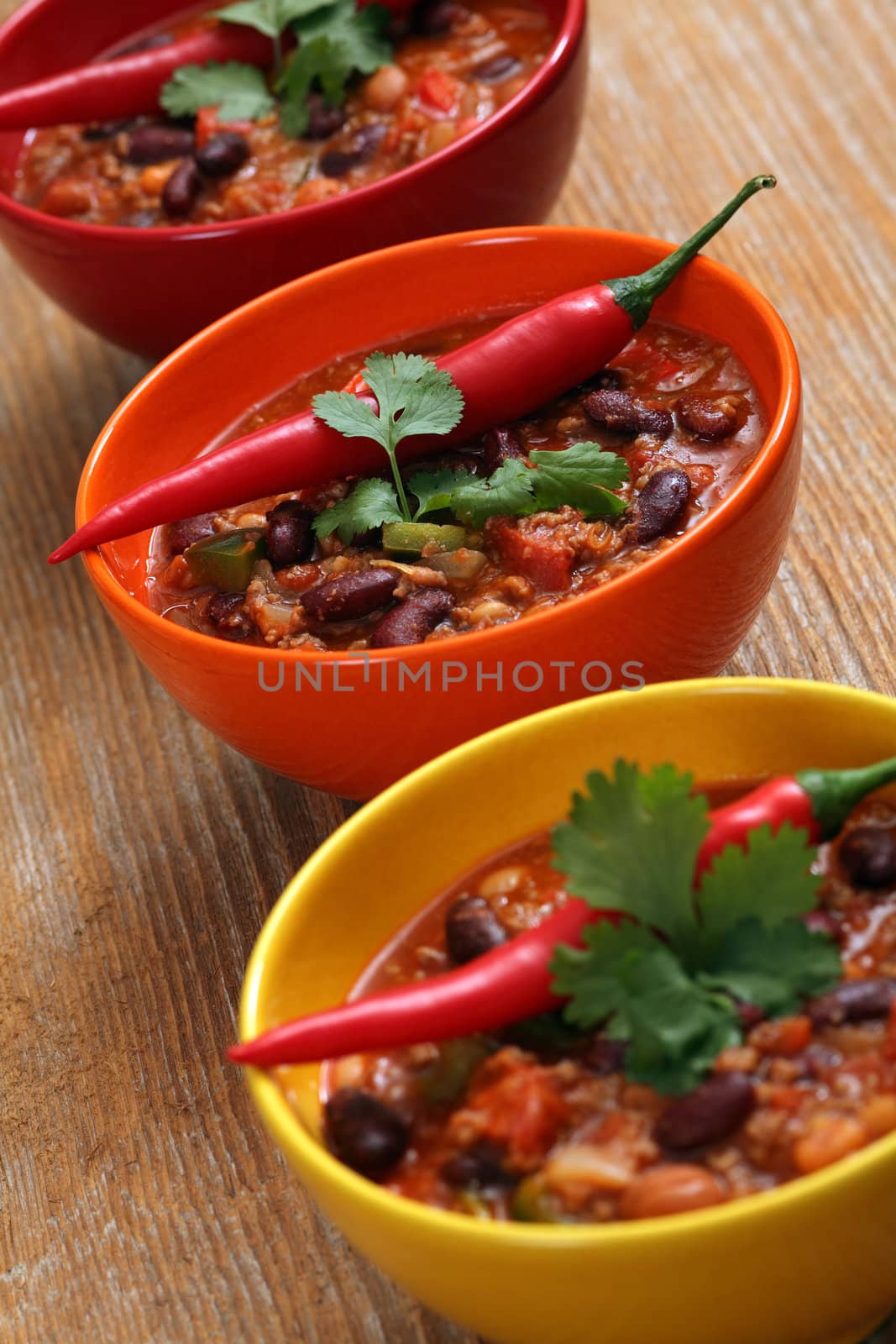 Photo of three bowls of chili resting on an old wood table.