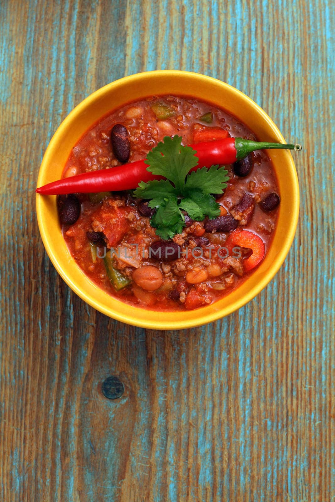Photo of a bowl of chili resting on an old wood table.